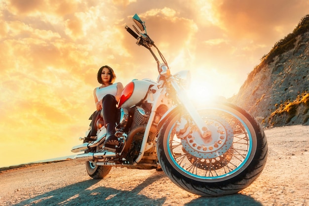 Une belle femme confiante pose assis sur une moto dans le contexte d'un coucher de soleil épique b