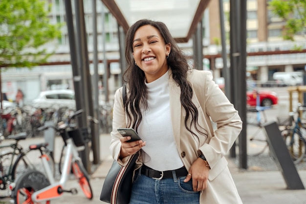 Belle femme confiante avec un visage émotionnel tenant un téléphone portable regardant la caméra dans la rue