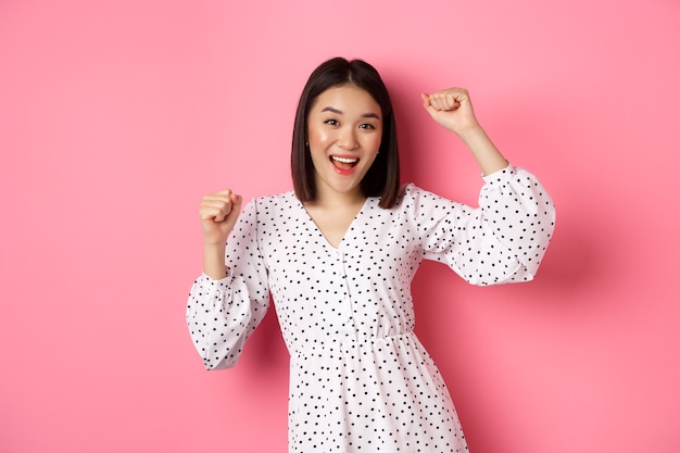 Belle femme coréenne dansant et s'amusant, souriante heureuse à la caméra, posant sur fond rose