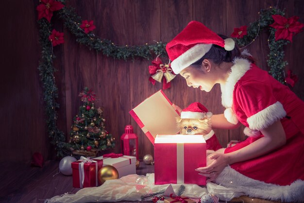 Une belle femme en costume de père Noël et des chiots mignons de Poméranie était ravie en ouvrant la boîte-cadeau le joyeux Noël et la bonne année.