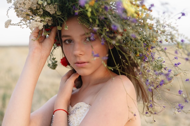 Belle femme avec une couronne sur la tête assise dans un champ de fleurs. Le concept de beauté, de vie libre et de naturel