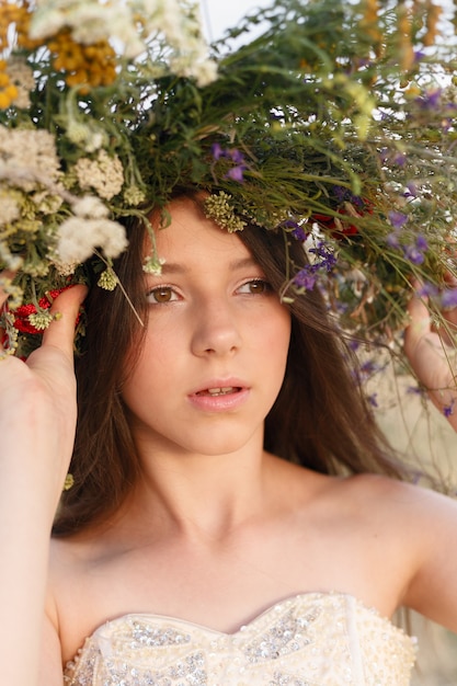 Belle femme avec une couronne sur la tête assise dans un champ de fleurs. Le concept de beauté, de vie libre et de naturel