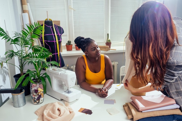 Belle femme couturière aux cheveux longs et tailleur client afro crée une image pour elle dans la maison de couture de l'atelier de couture