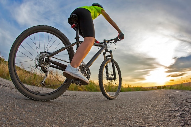 Belle femme cycliste fait du vélo sur la route au coucher du soleil. Mode de vie sain et sport. Loisirs et passe-temps