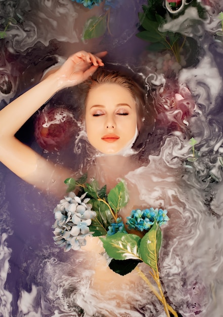 Belle femme dans la baignoire avec des fleurs et de l'eau violette