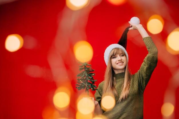 Une belle femme dans un bonnet de Noel tient un petit arbre de Noël dans ses mains Concept de nouvel an