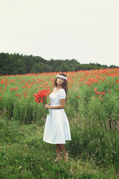 Belle femme dans un champ avec beaucoup de fleurs de pavot