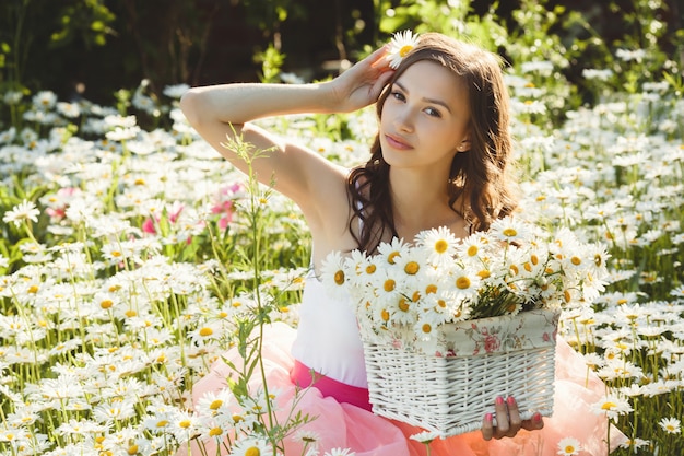 Belle femme dans le champ de camomille en été. Jolie fille avec bouquet de camomille dans le panier