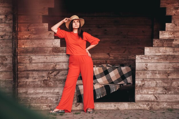 Belle femme dans un chapeau de paille vêtu de vêtements rouges se dresse sur le fond d'une maison en bois