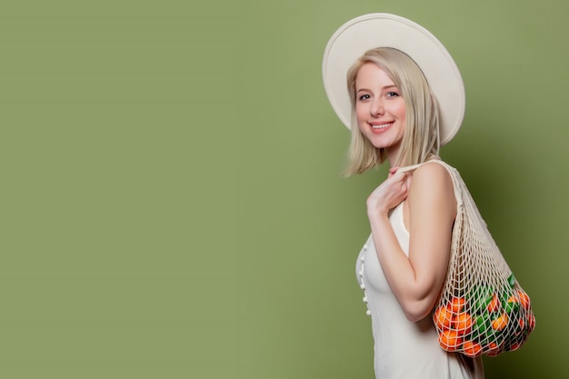 Belle femme dans un chapeau et une robe blanche avec un mandarins