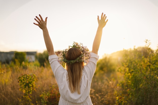 Belle femme dans une couronne de fleurs sauvages debout dans le champ de fleurs les mains sur le côté