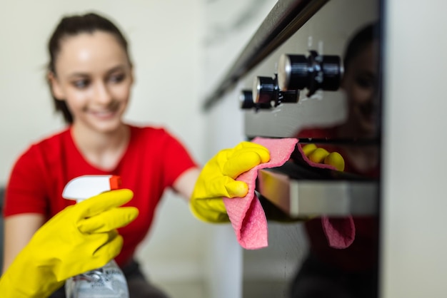 Belle femme dans des gants de protection nettoyant le four de cuisine dans la cuisine