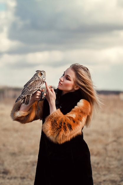 Belle femme dans un manteau de fourrure avec un hibou sur son bras.