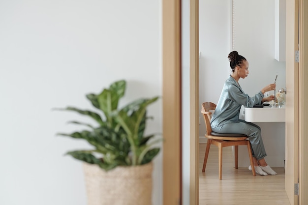 Belle femme dans un miroir grossissant de réglage de vêtements de détente à la vanité dans sa chambre