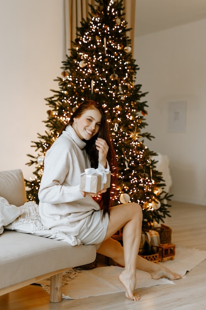 Belle femme dans un pull d'hiver blanc sur le fond d'un arbre de Noël