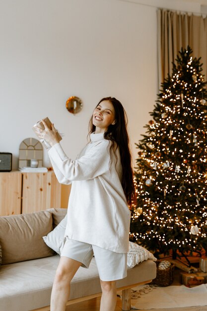 Belle femme dans un pull d'hiver blanc sur le fond d'un arbre de Noël