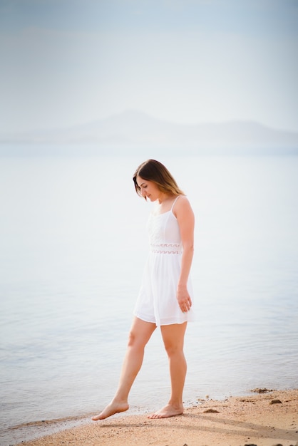 Belle femme dans une robe blanche marchant sur la plage.Femme détendue respirant l'air frais, femme sensuelle émotionnelle près de la mer, profitant de l'été.Voyages et vacances. Concept de liberté et d'inspiration