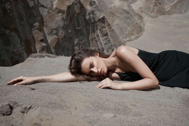 Belle femme dans une robe noire pose près des montagnes de sable