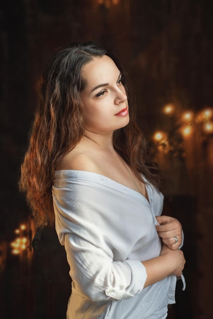 Belle femme dans un studio sombre dans une chemise blanche se présentant à la caméra