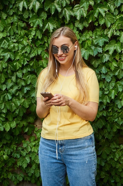 Belle femme dans un t-shirt jaune utilise un téléphone portable avec un casque pour les appels vidéo en écoutant de la musique