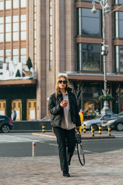 belle femme dans des vêtements décontractés à la mode se promenant dans la ville avec un smartphone à la main
