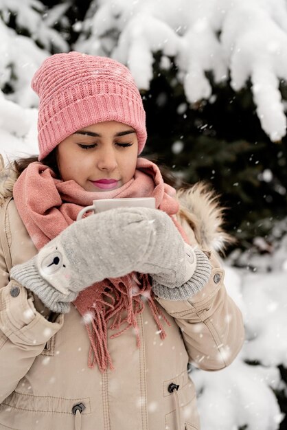 Belle femme dans des vêtements d'hiver chauds tenant une tasse buvant du thé ou du café chaud à l'extérieur par temps de neige