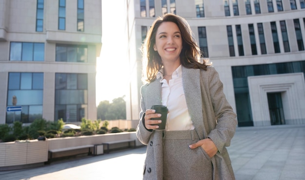 Belle femme debout avec un café près d'un immeuble de bureaux Portrait d'une femme réussie tenant une tasse de boisson chaude