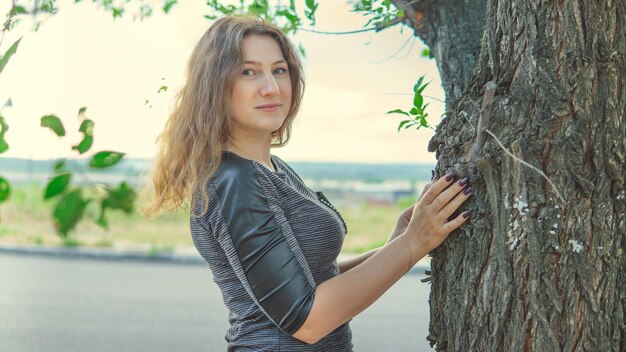 Belle femme debout près d'un arbre et regardant la caméra