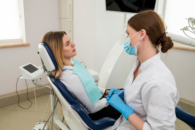 Une belle femme dentiste parle à un patient assis sur une chaise Explication conseil de consultation recommandation d'un dentiste