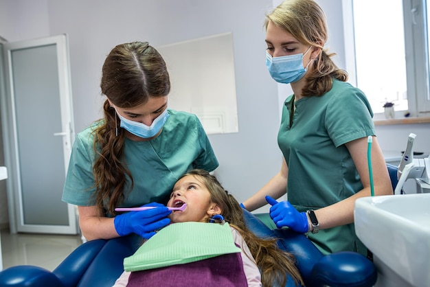 Belle femme dentiste avec son assistante en uniforme médical regardant les dents des enfants Le concept de traitement des dents des enfants