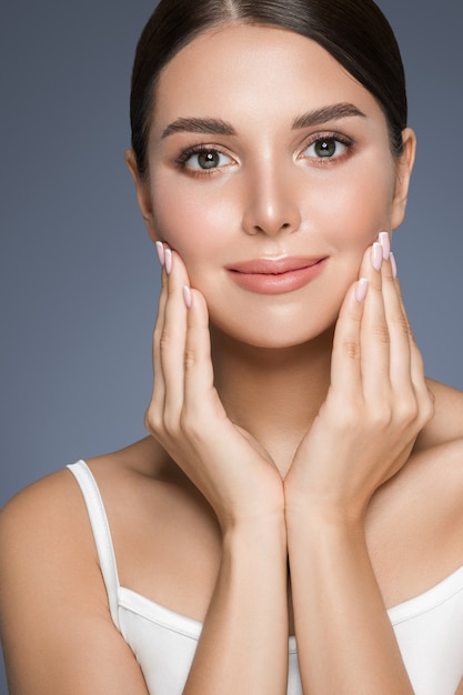 Belle femme avec des dents saines sourire portrait de peau propre et fraîche. Tournage en studio. Fond gris.