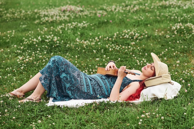 Belle femme détendue allongée sur l'herbe un jour d'été à jouer du ukulélé.