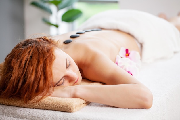 Belle femme de détente dans le salon spa avec des pierres chaudes sur le corps