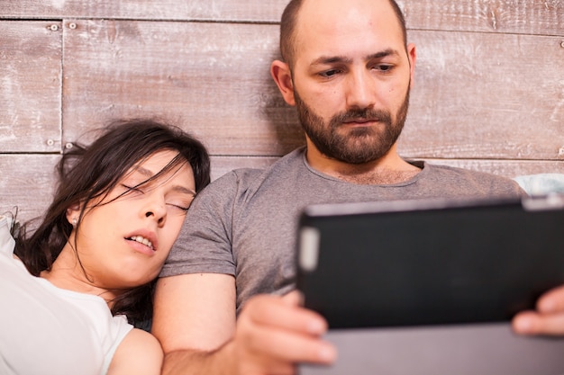 Photo belle femme dormant sur son mari mari pendant qu'il travaille tard sur une tablette.