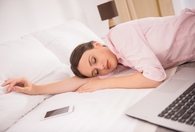 Belle femme dort sur le lit avec ordinateur portable et téléphone.