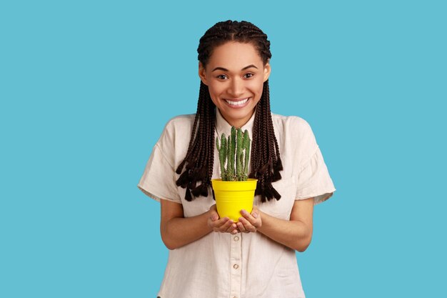 Belle femme avec des dreadlocks noirs transportant des cactus en pot dans son jardin sourit heureux