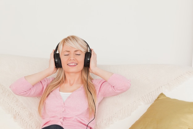 Belle femme écoute de la musique sur ses écouteurs tout en étant assis sur un canapé