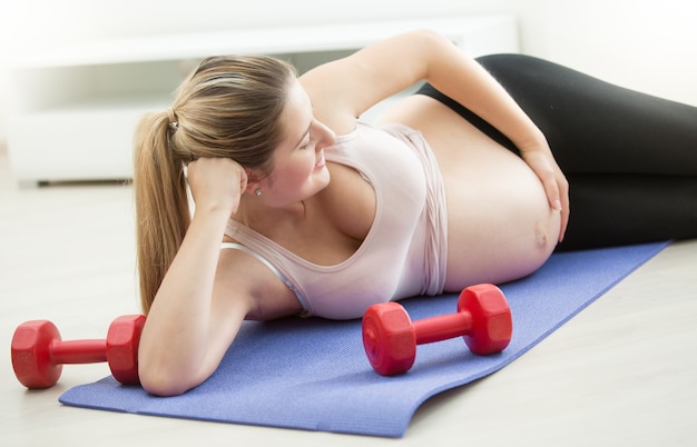 Belle femme enceinte allongée sur un tapis de fitness et touchant le gros ventre