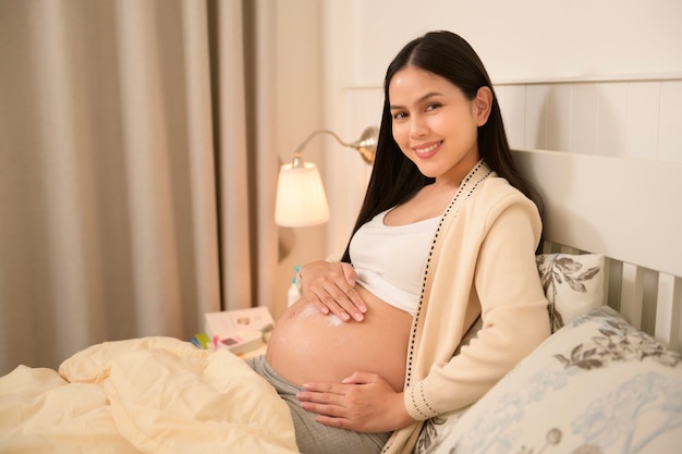 Une belle femme enceinte applique de la crème hydratante pour les verrues sur le ventre.