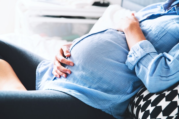 Belle femme enceinte assise au lit et tient les mains sur le ventre dans la chambre à la maison