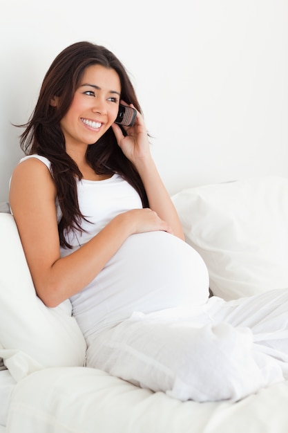 Belle femme enceinte au téléphone en position couchée sur un lit