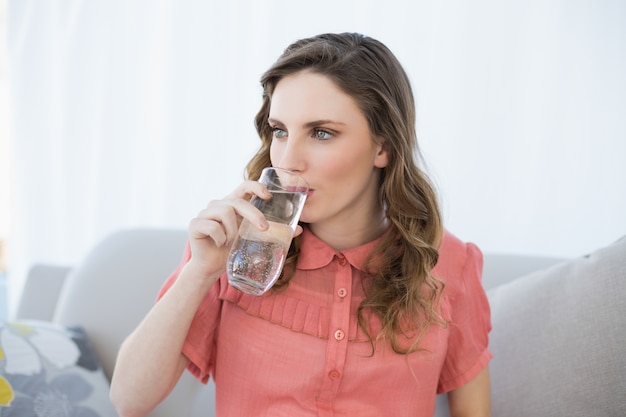 Belle femme enceinte, boire un verre d&#39;eau assis sur le canapé dans le salon