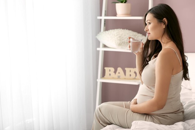 Belle femme enceinte buvant de l'eau dans la chambre