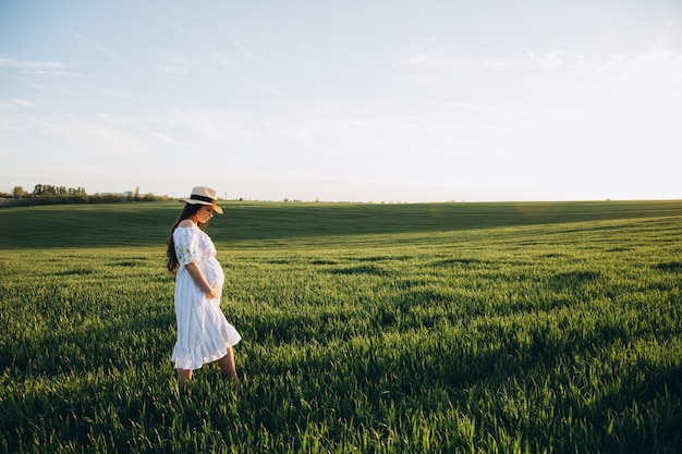 Belle femme enceinte dans le champ de la nature au printemps au coucher du soleil