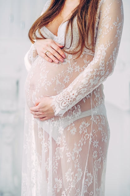 Belle femme enceinte dans un peignoir de dentelle blanche tenant sur le ventre de femme enceinte