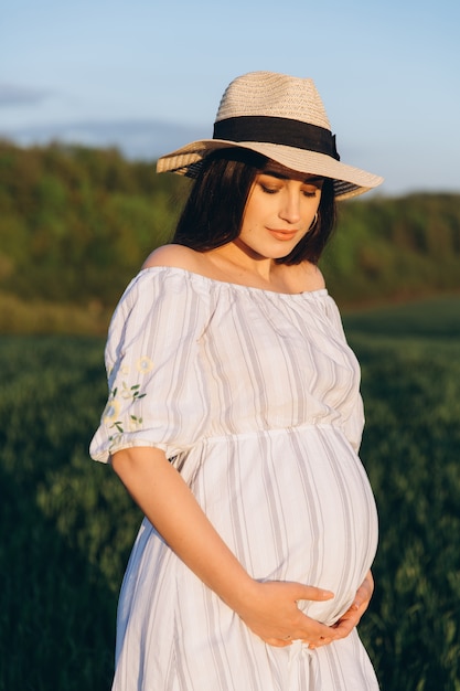 Belle femme enceinte dans le pré nature d'été au coucher du soleil