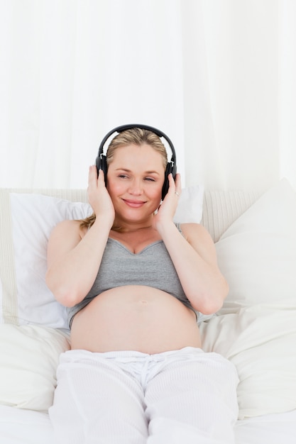 Belle femme enceinte en écoutant de la musique sur son lit