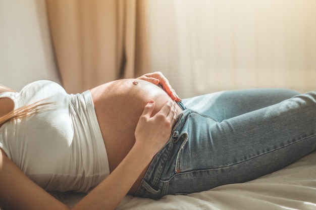 Belle femme enceinte est allongée sur le lit et se tient par le ventre. Relaxation. Concept de grossesse