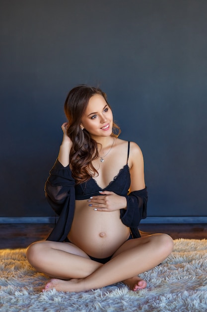 Belle femme enceinte heureuse assis dans ses sous-vêtements sur le sol