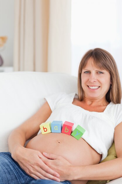 Belle femme enceinte jouant avec des blocs de bois en position couchée sur un canapé